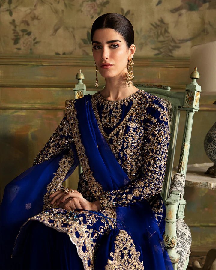 Model wearing a royal blue Seyhana dress with intricate gold embroidery from Faiza Saqlain's Luxe Formals Manaar Nov '23 collection. Pakistani clothes online in UK.