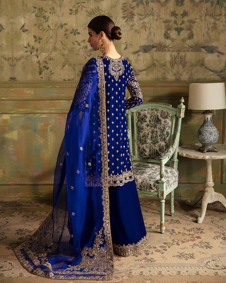 Model wearing a royal blue Seyhana dress with intricate gold embroidery from Faiza Saqlain's Luxe Formals Manaar Nov '23 collection. Pakistani clothes online in UK.