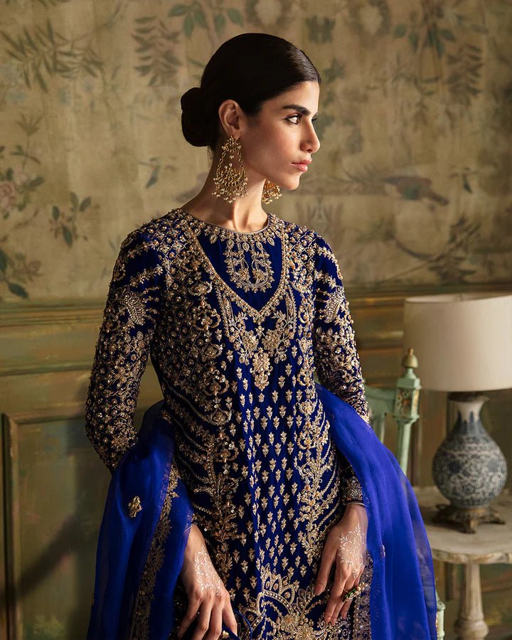 Model wearing a royal blue Seyhana dress with intricate gold embroidery from Faiza Saqlain's Luxe Formals Manaar Nov '23 collection. Pakistani clothes online in UK.