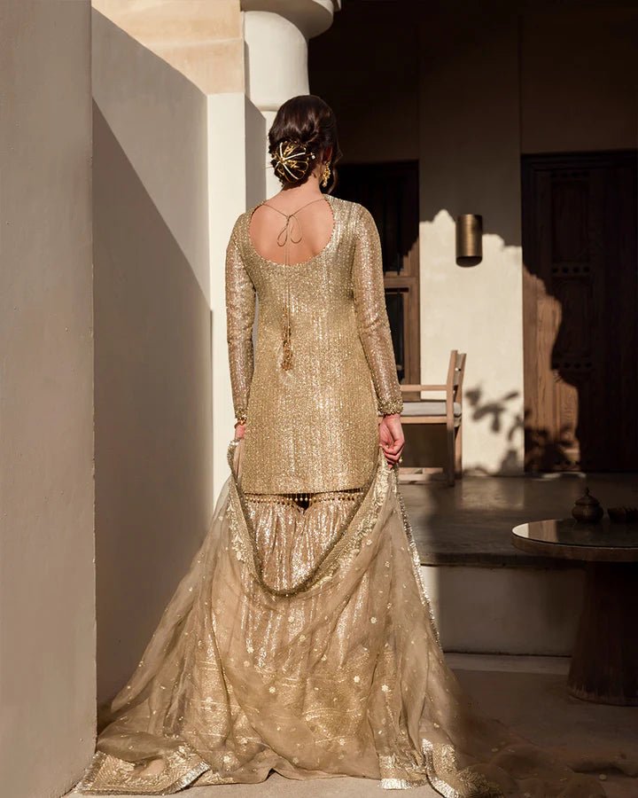 Model wearing a gold Linia dress with intricate embellishments from Faiza Saqlain's Aleira Evening Edit '24 collection. Pakistani clothes online in UK.