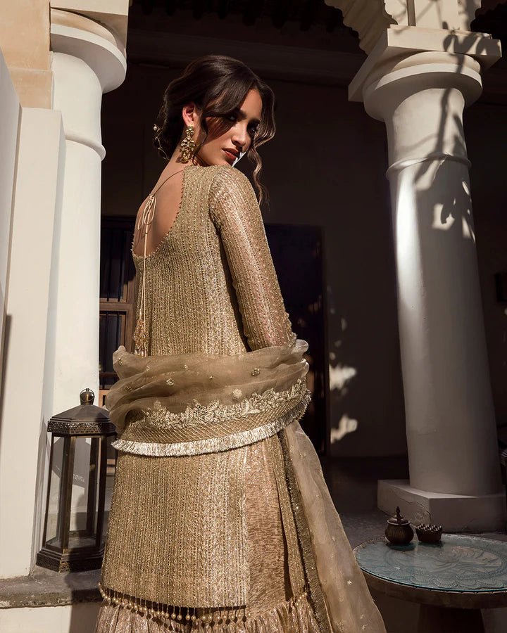 Model wearing a gold Linia dress with intricate embellishments from Faiza Saqlain's Aleira Evening Edit '24 collection. Pakistani clothes online in UK.