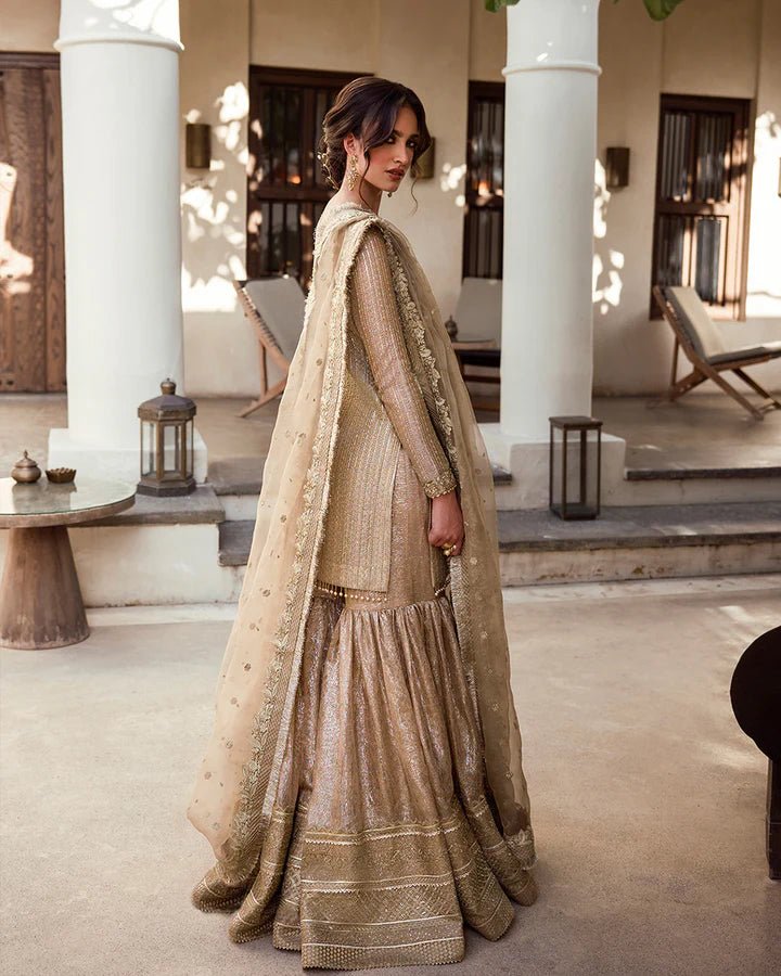 Model wearing a gold Linia dress with intricate embellishments from Faiza Saqlain's Aleira Evening Edit '24 collection. Pakistani clothes online in UK.