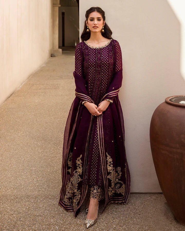 Model wearing a deep purple Yashal dress adorned with golden embroidery from Faiza Saqlain's Luxe Formals Noor e Chashm collection. Pakistani clothes online in UK.