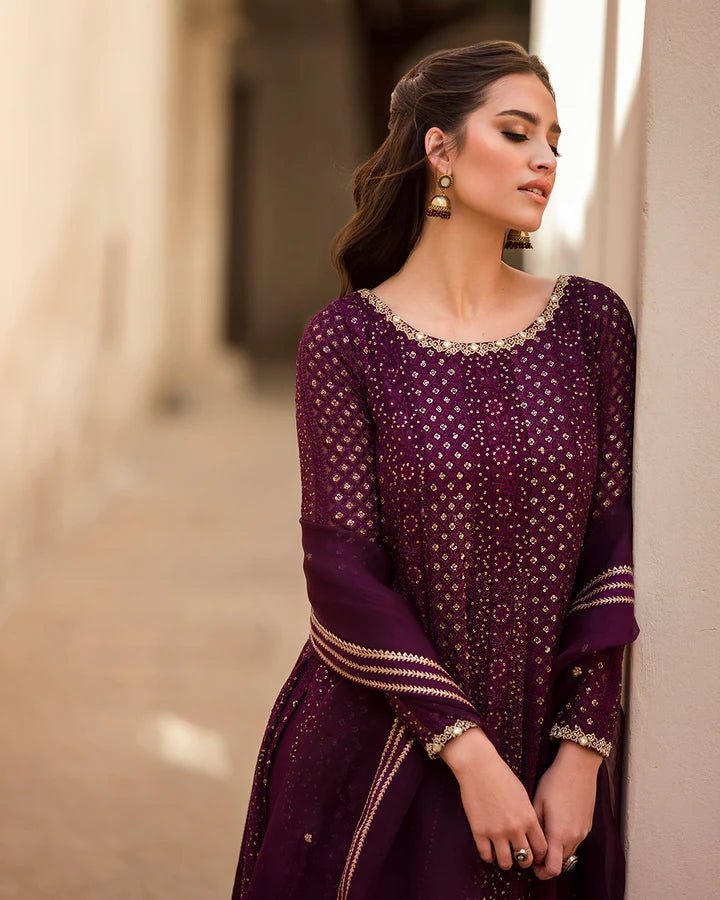 Model wearing a deep purple Yashal dress adorned with golden embroidery from Faiza Saqlain's Luxe Formals Noor e Chashm collection. Pakistani clothes online in UK.