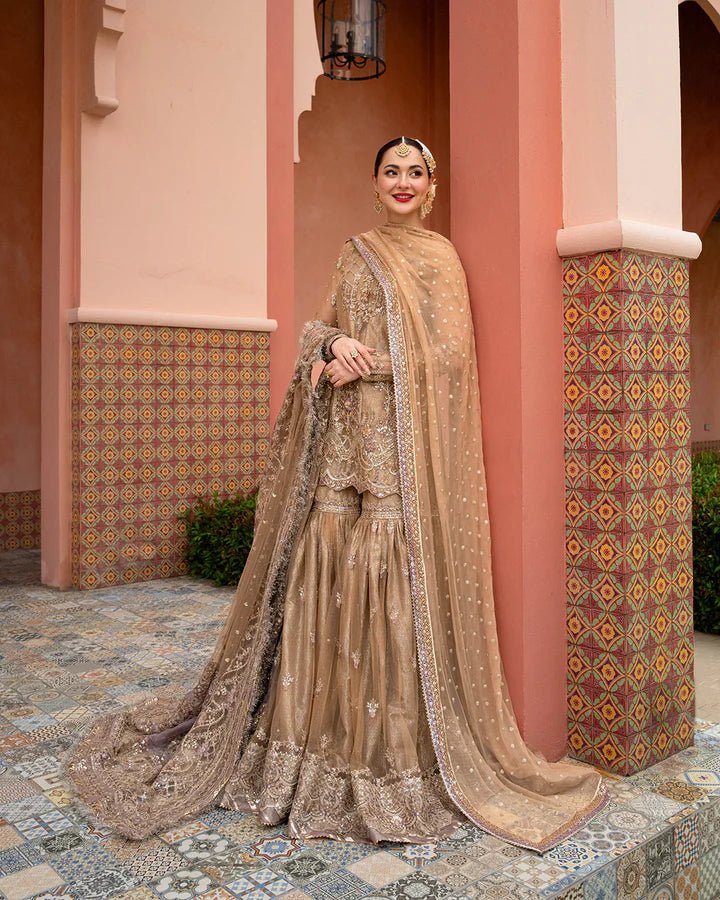 Model wearing a gold Jolina dress from Faiza Saqlain's Neorah Wedding Festive '24 Collection, featuring intricate embroidery and a flowing silhouette. Pakistani wedding clothes available online in the UK.