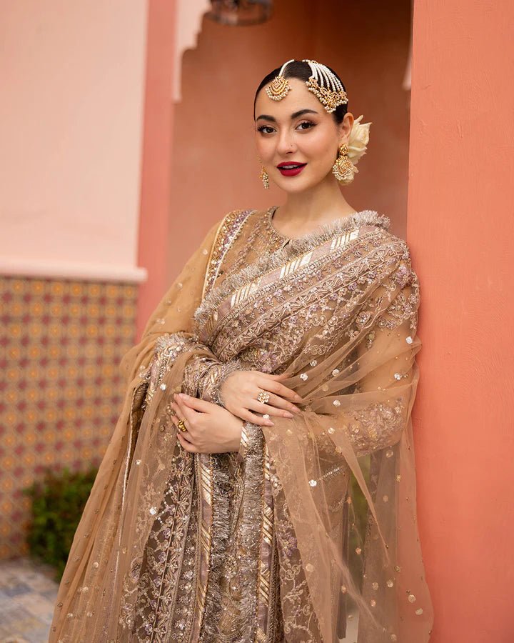 Model wearing a gold Jolina dress from Faiza Saqlain's Neorah Wedding Festive '24 Collection, featuring intricate embroidery and a flowing silhouette. Pakistani wedding clothes available online in the UK.