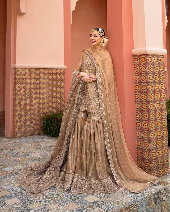 Model wearing a gold Jolina dress from Faiza Saqlain's Neorah Wedding Festive '24 Collection, featuring intricate embroidery and a flowing silhouette. Pakistani wedding clothes available online in the UK.