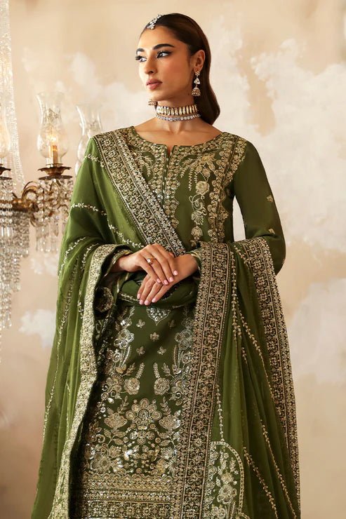 Model wearing an olive - green Gulaal Shehrnaaz Raw Silk outfit, embellished with intricate embroidery and sequins on the front, sleeves, and back. The look is completed with a fully embroidered chiffon dupatta and dyed silk trousers, ideal for festive occasions.