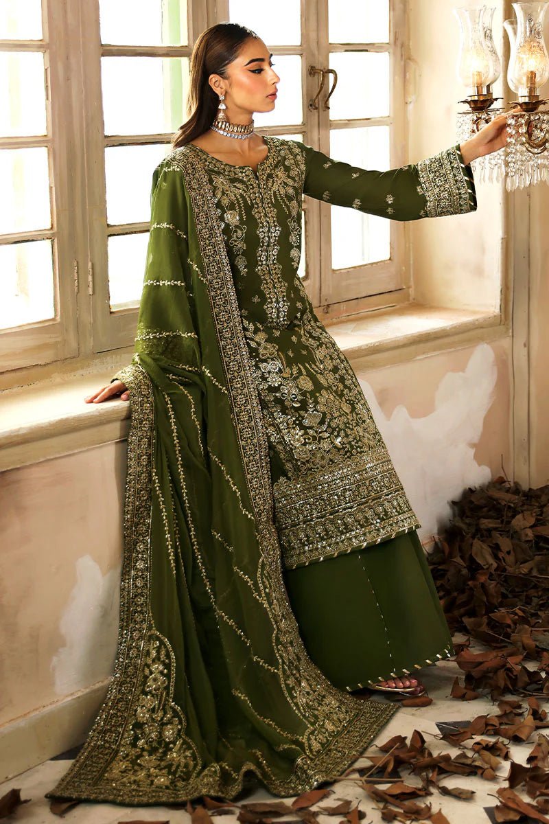 Model wearing an olive - green Gulaal Shehrnaaz Raw Silk outfit, embellished with intricate embroidery and sequins on the front, sleeves, and back. The look is completed with a fully embroidered chiffon dupatta and dyed silk trousers, ideal for festive occasions.