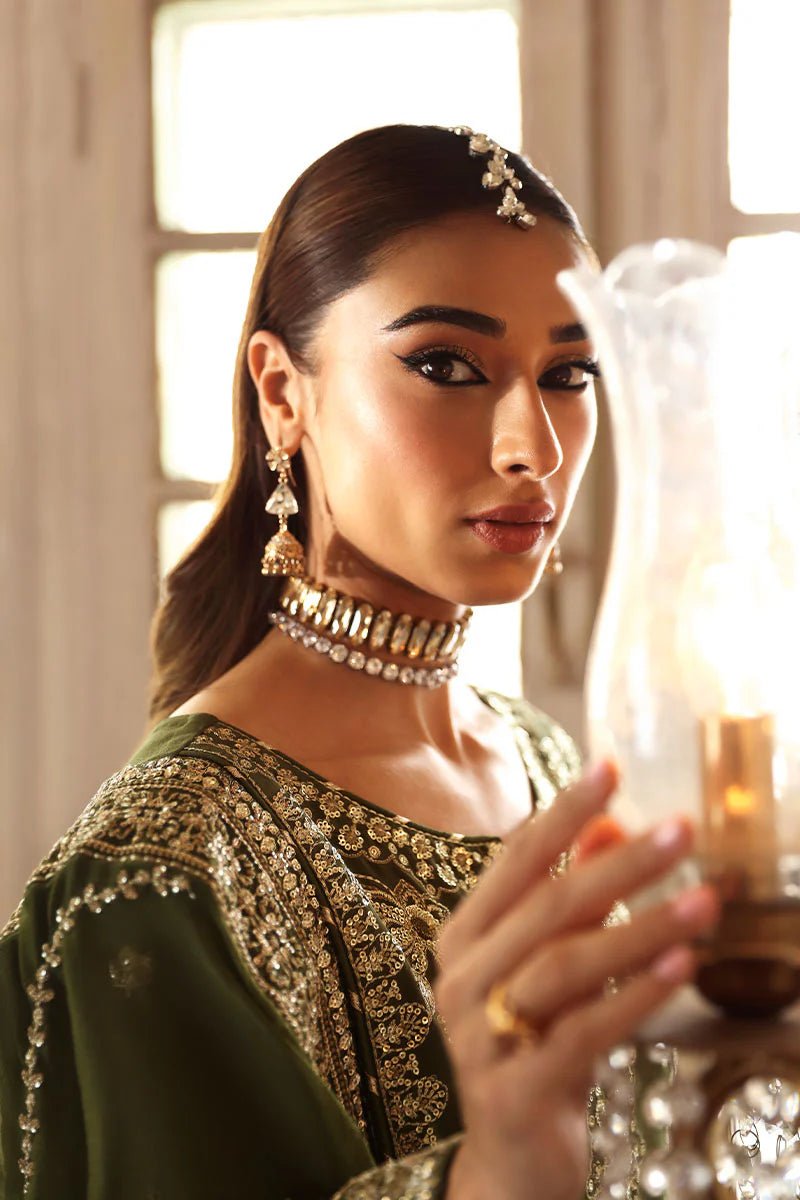 Model wearing an olive - green Gulaal Shehrnaaz Raw Silk outfit, embellished with intricate embroidery and sequins on the front, sleeves, and back. The look is completed with a fully embroidered chiffon dupatta and dyed silk trousers, ideal for festive occasions.