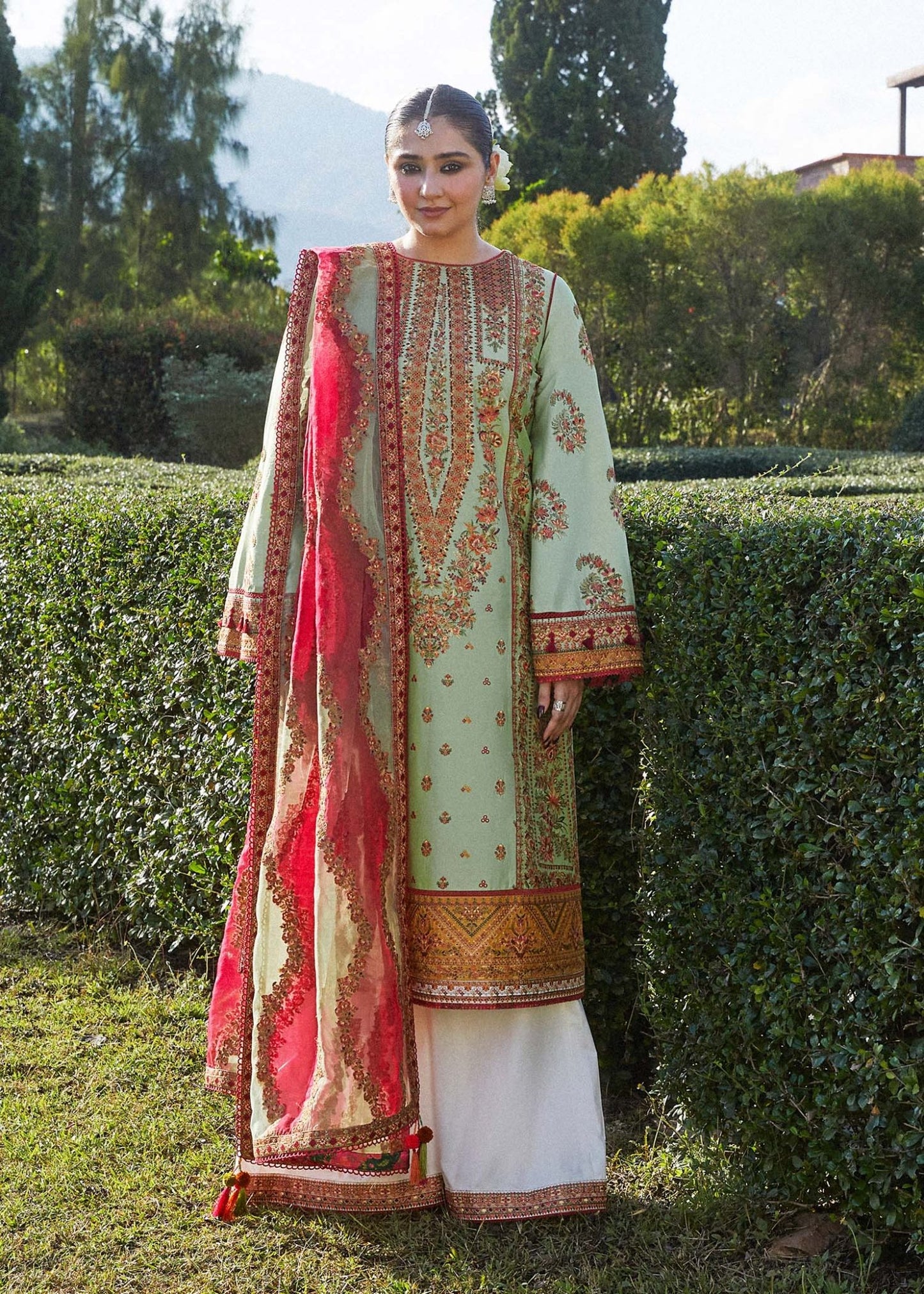 Model wearing Hussain Rehar Gul Bahar dress, sage green with red accents, Pakistani clothing UK.