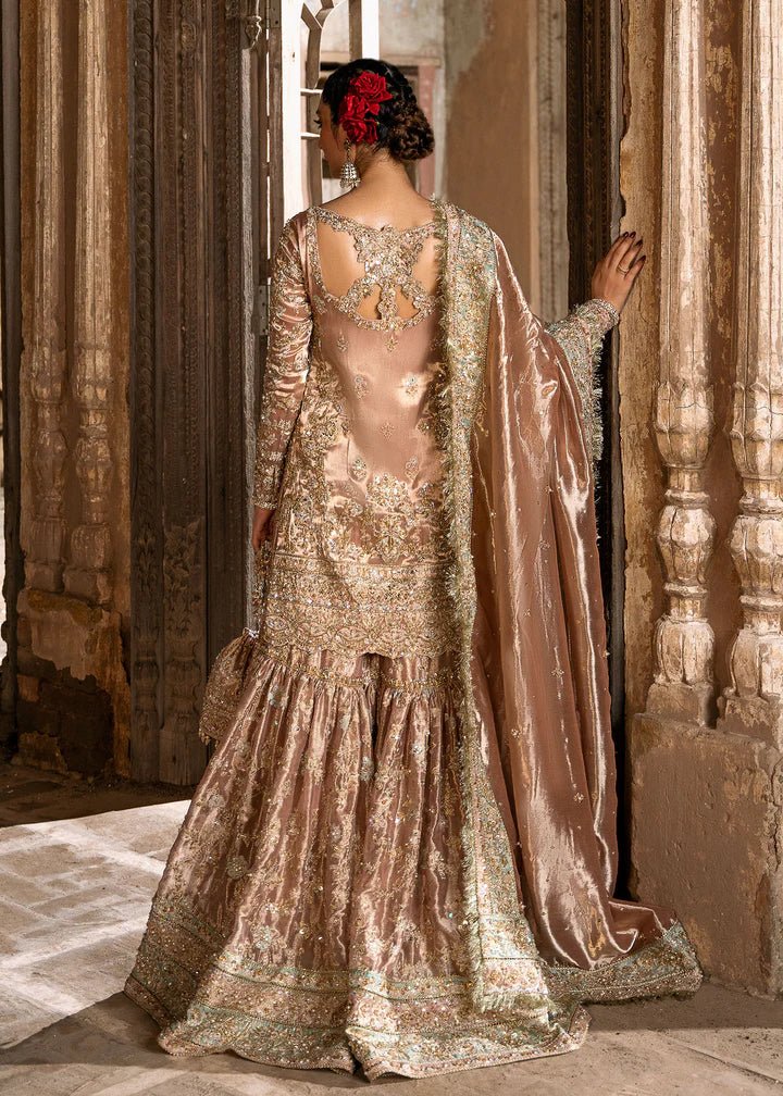 Model wearing a champagne - colored Meeram dress from Kanwal Malik's Sajni II Formal Collection, featuring intricate embroidery and velvet shawl. Pakistani wedding clothes available online in the UK.