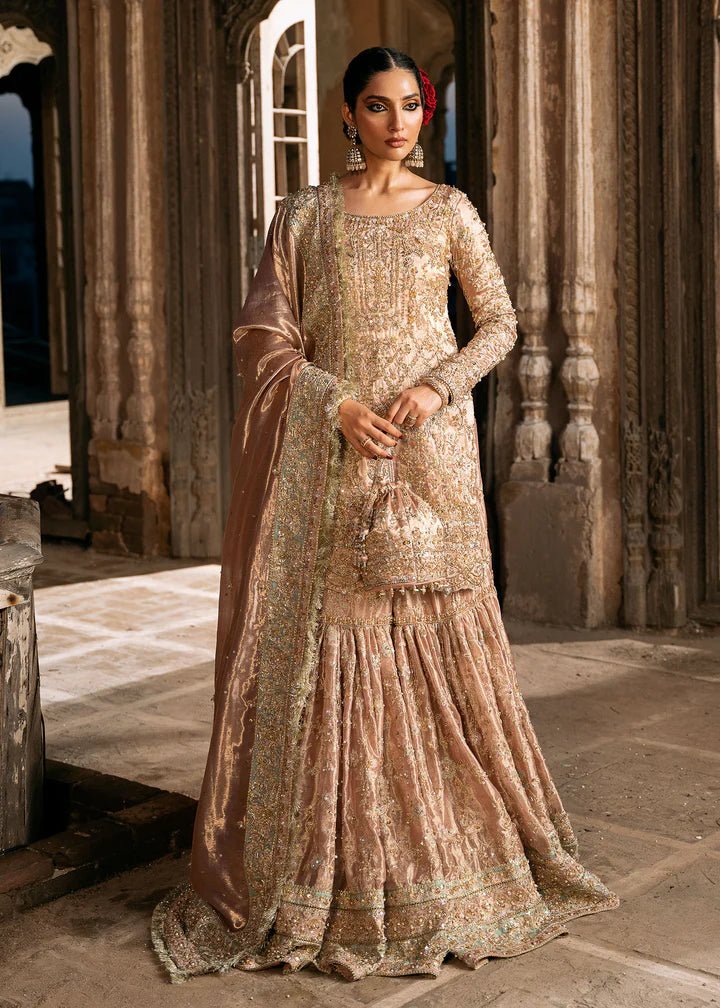 Model wearing a champagne - colored Meeram dress from Kanwal Malik's Sajni II Formal Collection, featuring intricate embroidery and velvet shawl. Pakistani wedding clothes available online in the UK.