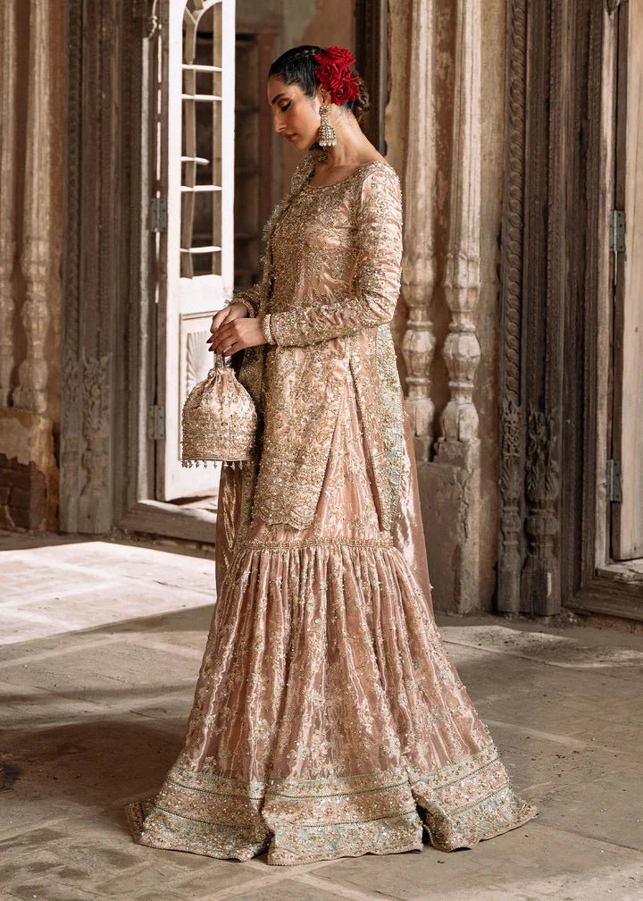 Model wearing a champagne - colored Meeram dress from Kanwal Malik's Sajni II Formal Collection, featuring intricate embroidery and velvet shawl. Pakistani wedding clothes available online in the UK.