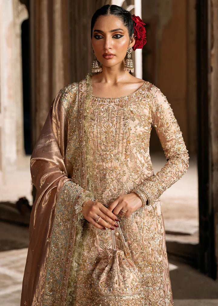 Model wearing a champagne - colored Meeram dress from Kanwal Malik's Sajni II Formal Collection, featuring intricate embroidery and velvet shawl. Pakistani wedding clothes available online in the UK.