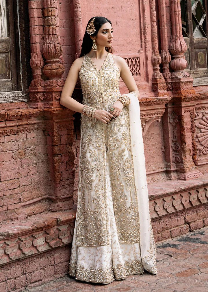 Model wearing an ivory Nisha dress from Kanwal Malik's Sajni II Formal Collection, detailed with intricate gold embroidery and paired with a matching dupatta. Pakistani wedding clothes available online in the UK.