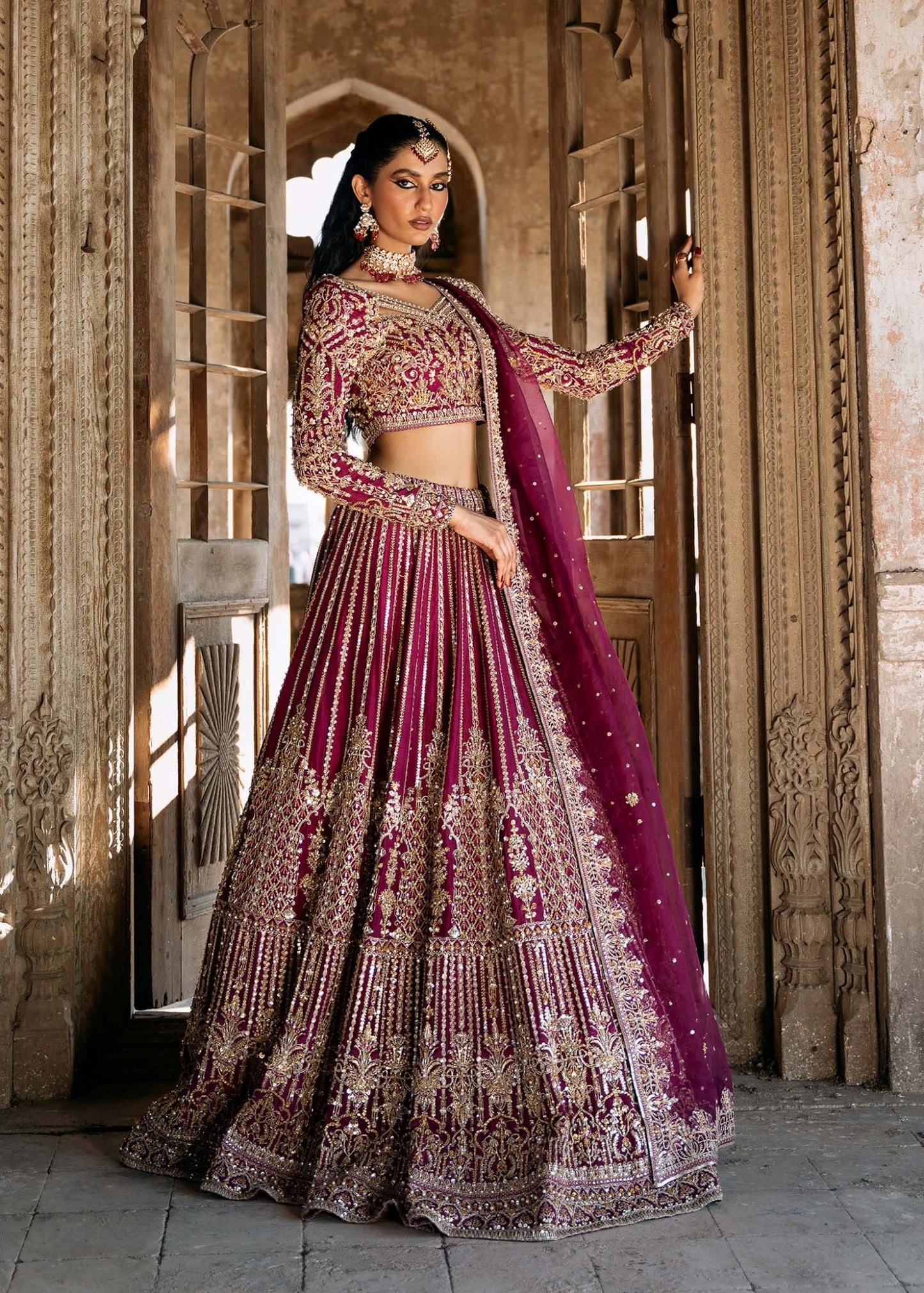 Model wearing a deep magenta and gold embellished Raina lehenga from Kanwal Malik's Sajni II collection. Pakistani wedding clothes online in the UK.