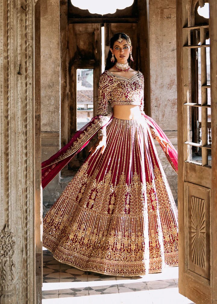 Model wearing a deep magenta and gold embellished Raina lehenga from Kanwal Malik's Sajni II collection. Pakistani wedding clothes online in the UK.