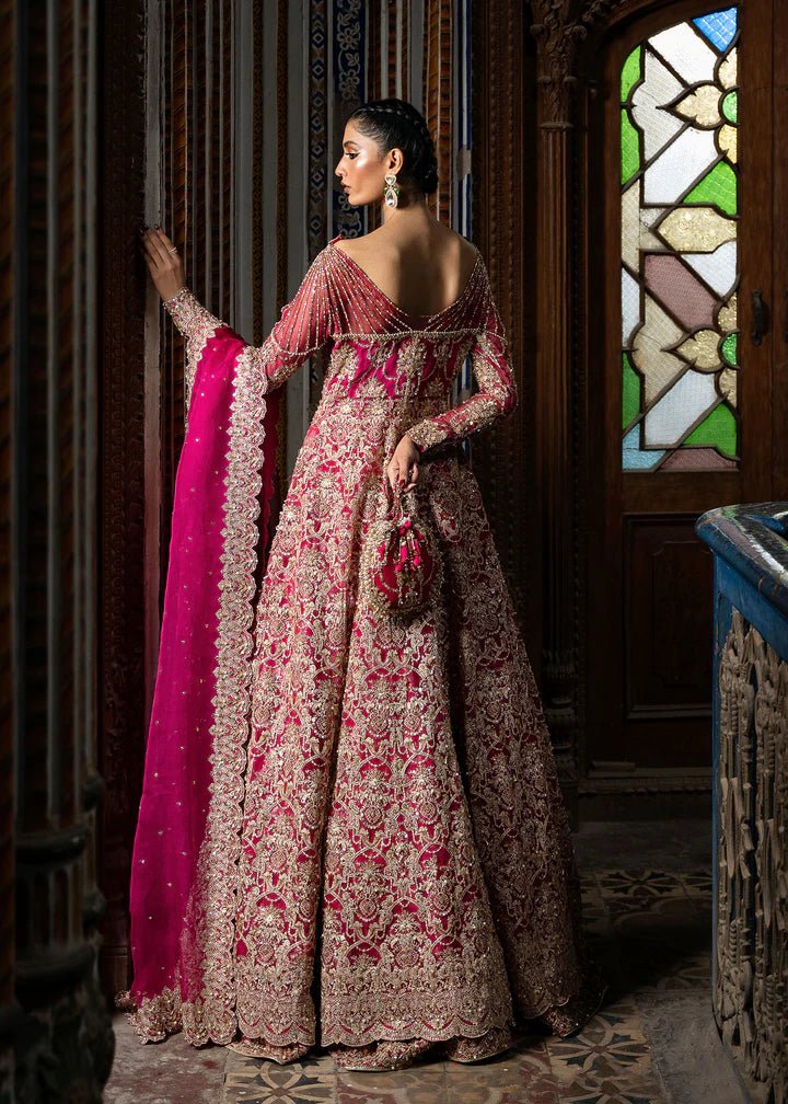 Model wearing a vibrant pink Sarosh dress from Kanwal Malik's Sajni II Formal Collection, adorned with intricate gold embroidery, paired with a matching dupatta. Pakistani wedding clothes available online in the UK.