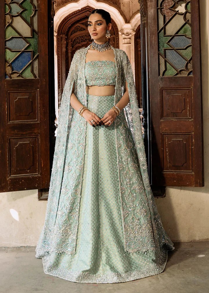 Model wearing a pastel green Shaqfaq dress from Kanwal Malik's Sajni II Formal Collection, featuring intricate embroidery and a matching cape. Pakistani wedding clothes available online in the UK.