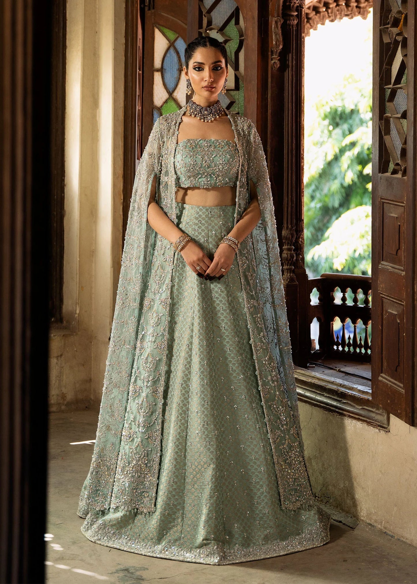 Model wearing a pastel green Shaqfaq dress from Kanwal Malik's Sajni II Formal Collection, featuring intricate embroidery and a matching cape. Pakistani wedding clothes available online in the UK.