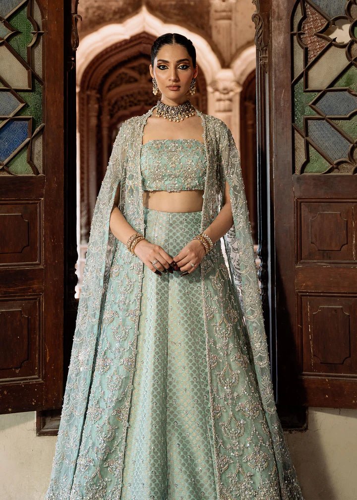 Model wearing a pastel green Shaqfaq dress from Kanwal Malik's Sajni II Formal Collection, featuring intricate embroidery and a matching cape. Pakistani wedding clothes available online in the UK.