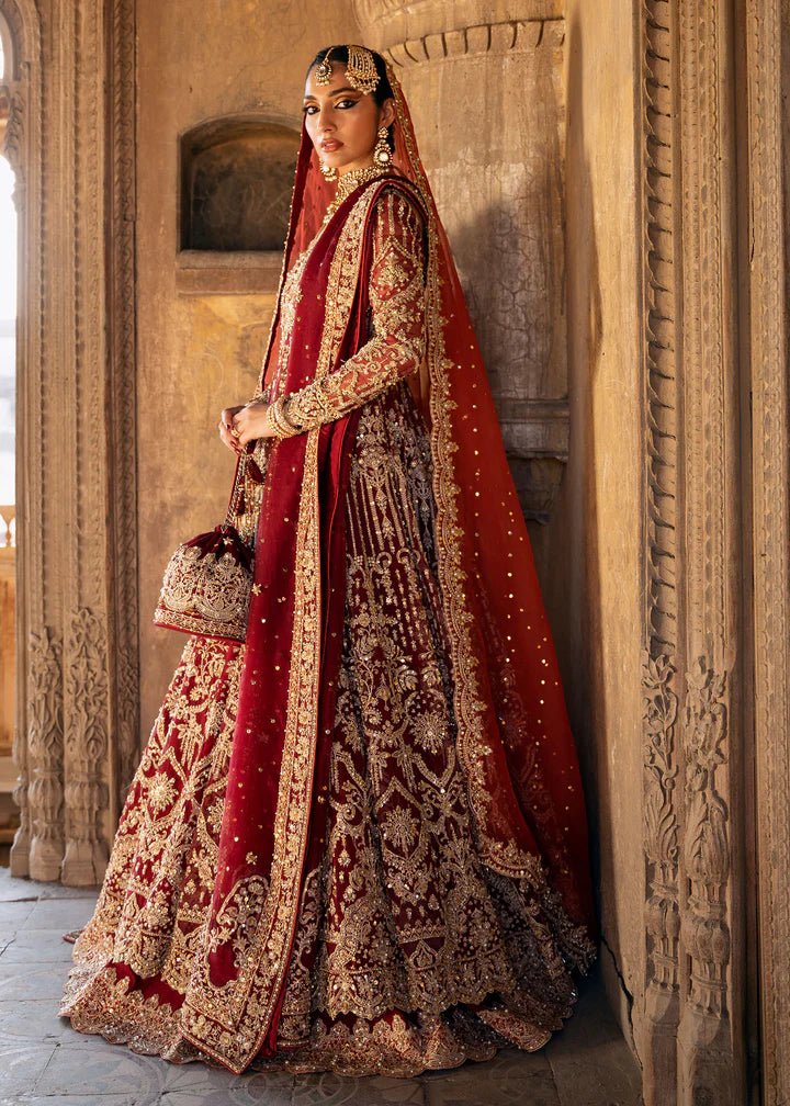 Model wearing a deep red Shirin lehenga from Kanwal Malik's Sajni II Formal Collection, intricately adorned with gold embroidery and paired with a matching dupatta. Pakistani wedding clothes available online in the UK.