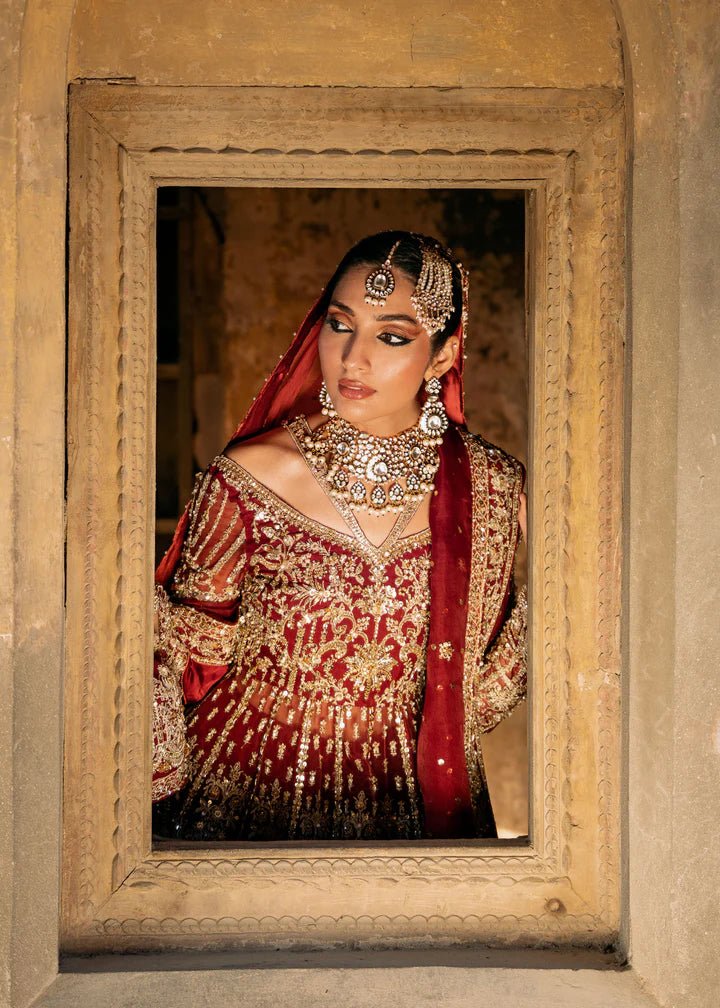 Model wearing a deep red Shirin lehenga from Kanwal Malik's Sajni II Formal Collection, intricately adorned with gold embroidery and paired with a matching dupatta. Pakistani wedding clothes available online in the UK.