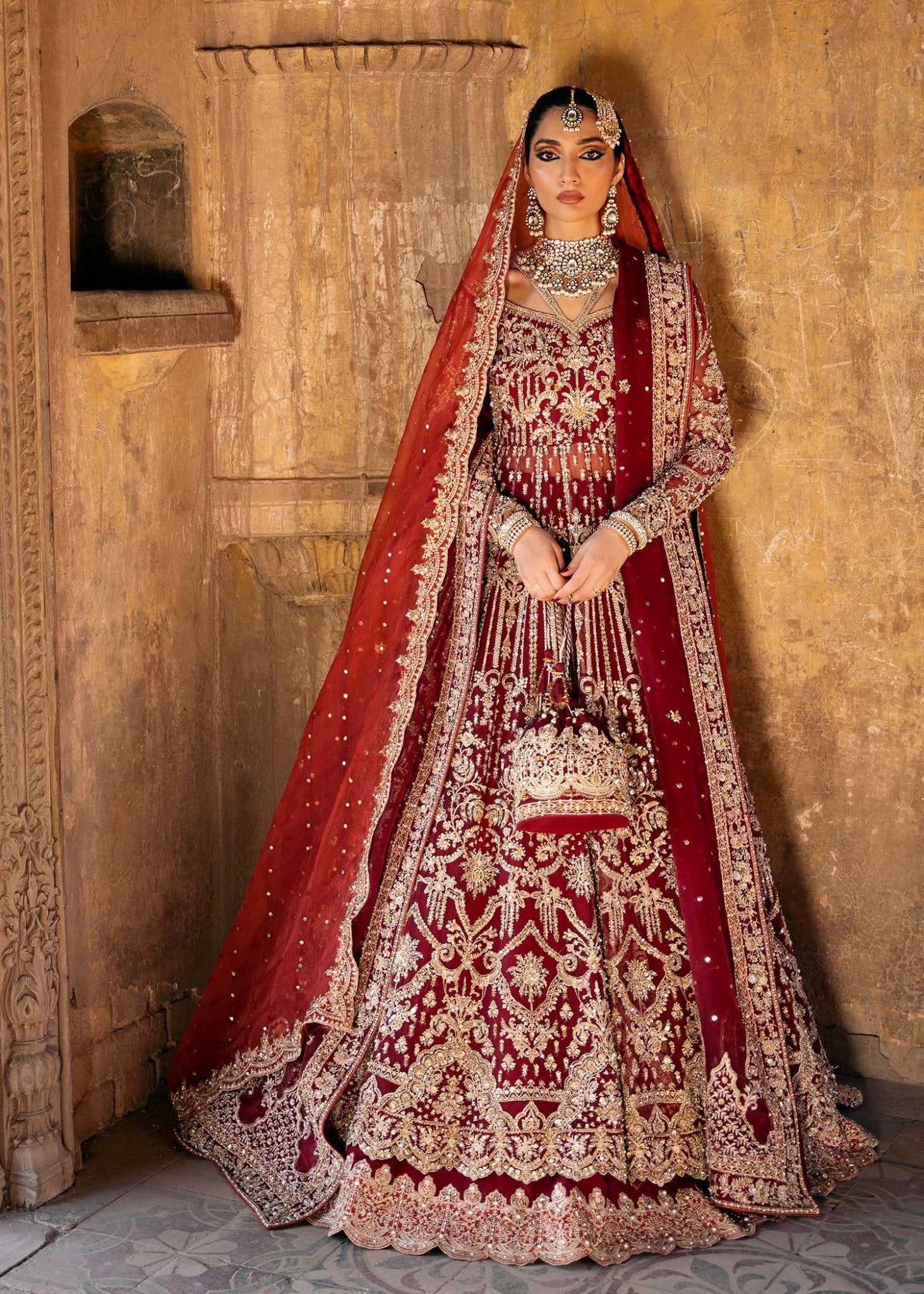 Model wearing a deep red Shirin lehenga from Kanwal Malik's Sajni II Formal Collection, intricately adorned with gold embroidery and paired with a matching dupatta. Pakistani wedding clothes available online in the UK.