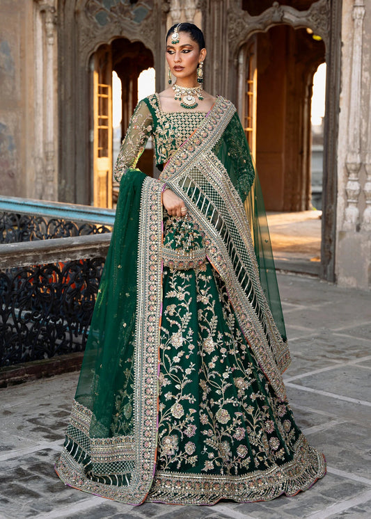 Model wearing a rich emerald green Sukhan lehenga from Kanwal Malik's Sajni II collection, embellished with intricate gold embroidery. Pakistani wedding clothes online in the UK.