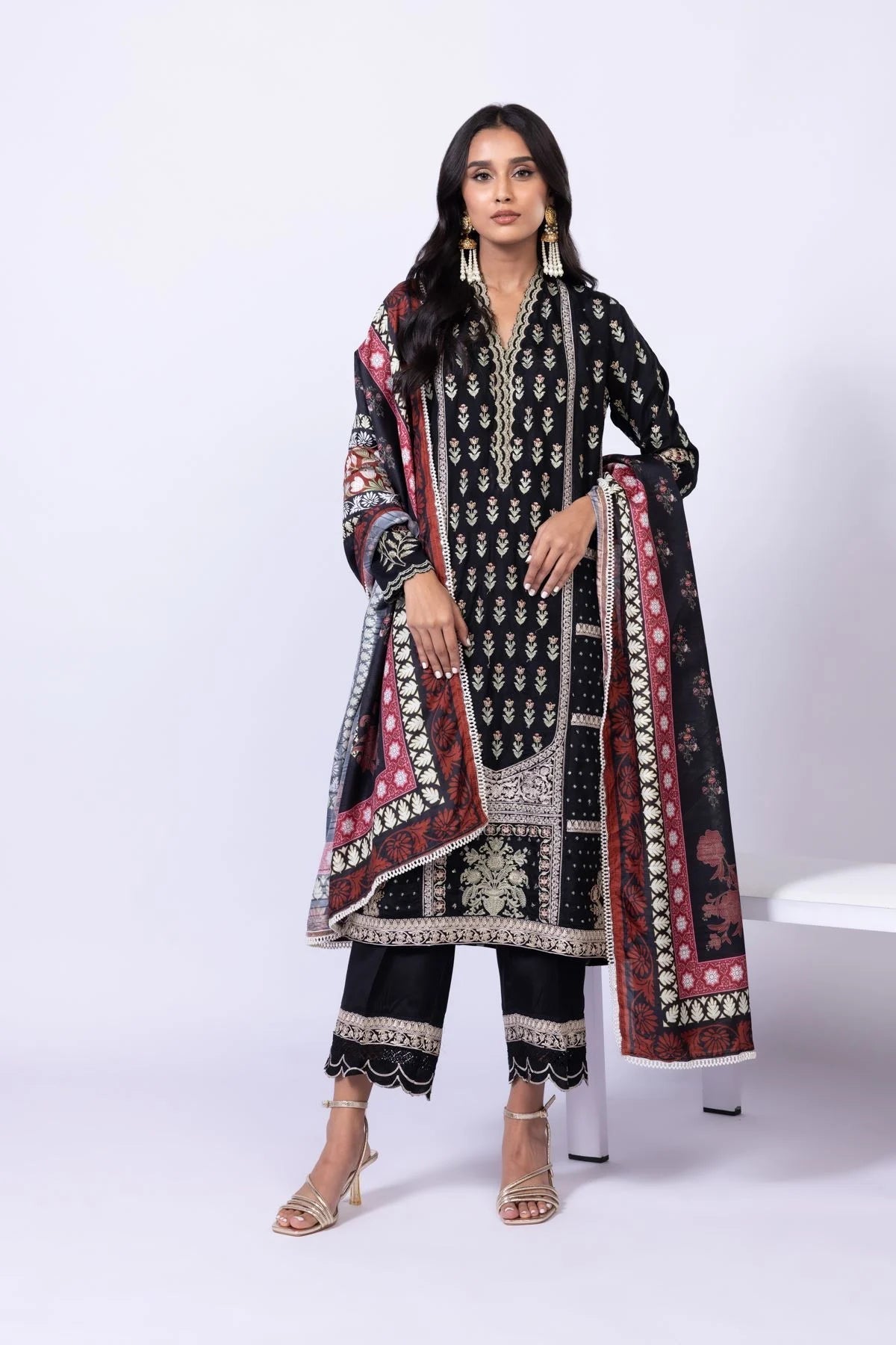 Model wearing Khaadi EST24610B black dress with intricate red and gold prints. Shop Pakistani clothes online in the UK now.