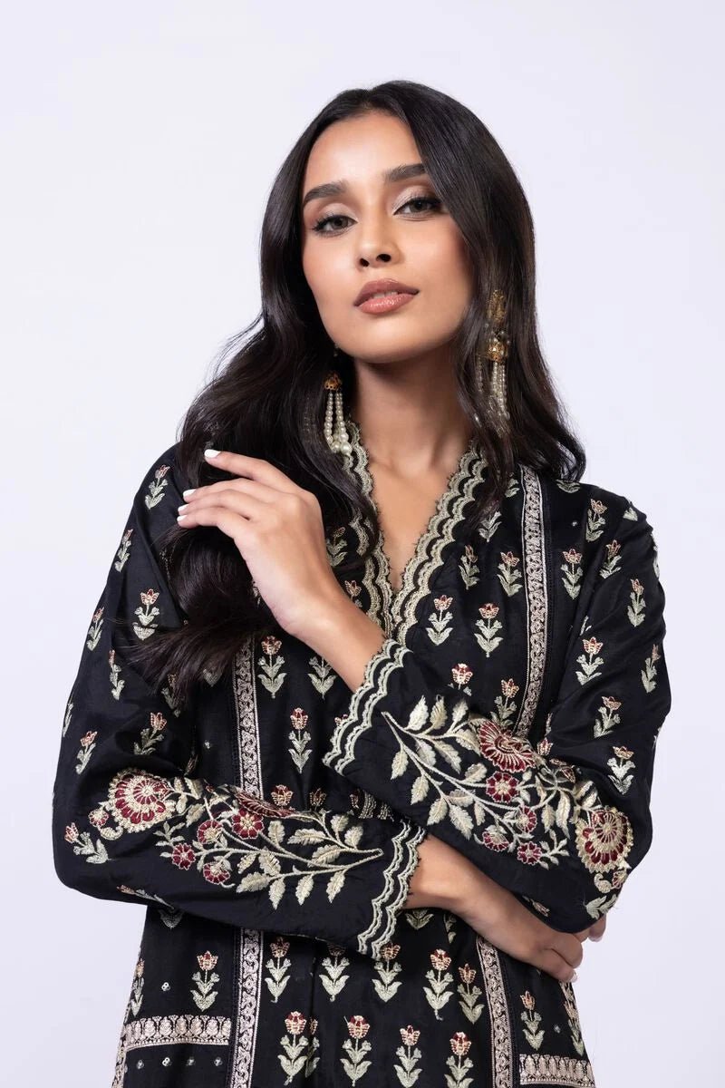 Model wearing Khaadi EST24610B black dress with intricate red and gold prints. Shop Pakistani clothes online in the UK now.