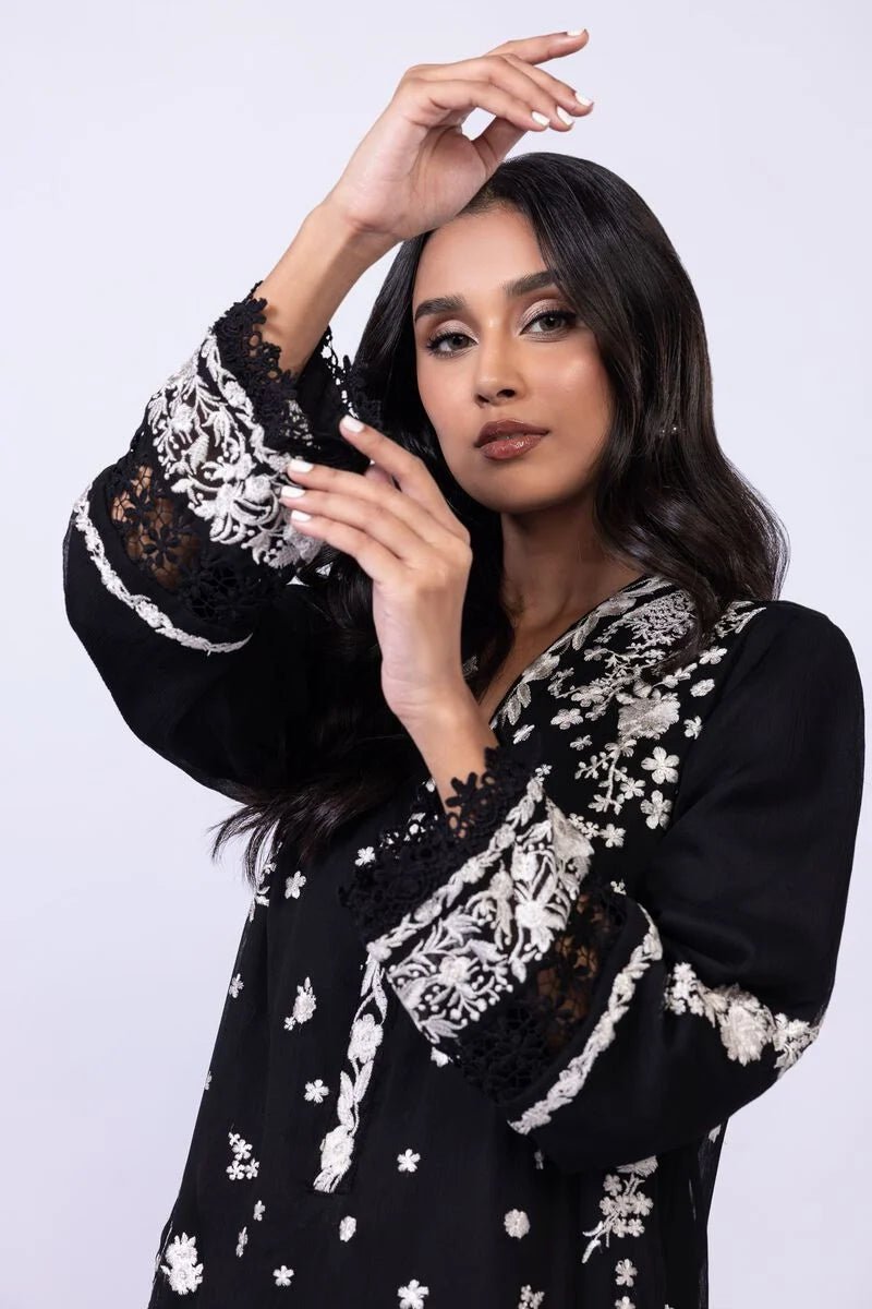 Model wearing Khaadi EST24633B black dress with elegant white embroidery and lace details. Shop Pakistani clothes online in the UK now.