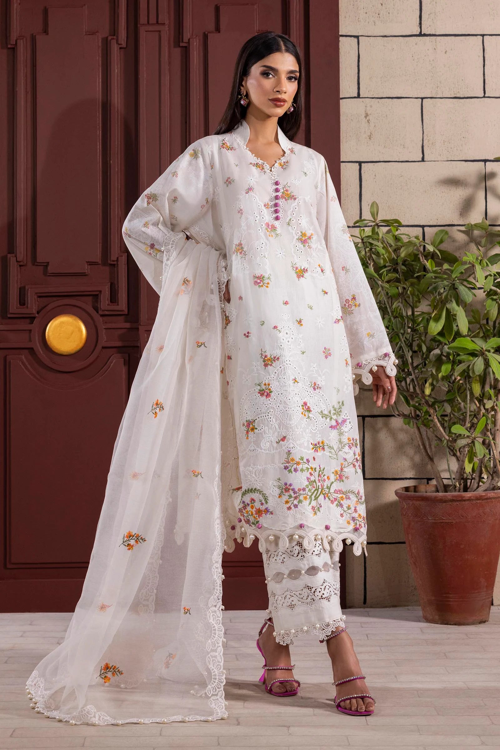 Model wearing white embroidered dress with multicolor floral accents and lace detailing from Sana Safinaz Muzlin Spring '25, Pakistani clothes online UK.