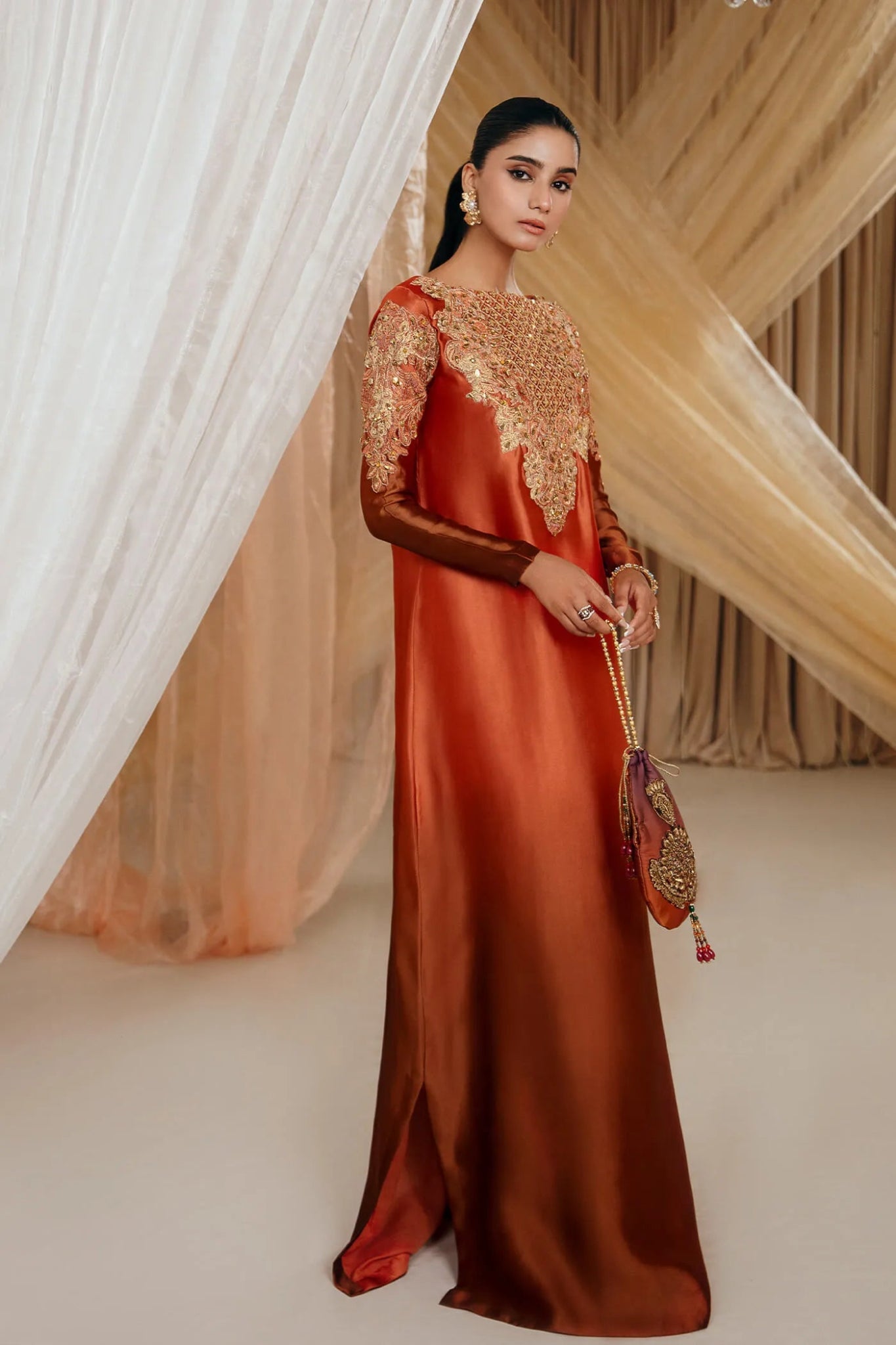 Model wearing a rust - colored SUNSET GLOW dress from Musferah Saad's MYSTERE Eid collection '24, showcasing Pakistani clothes online in the UK.