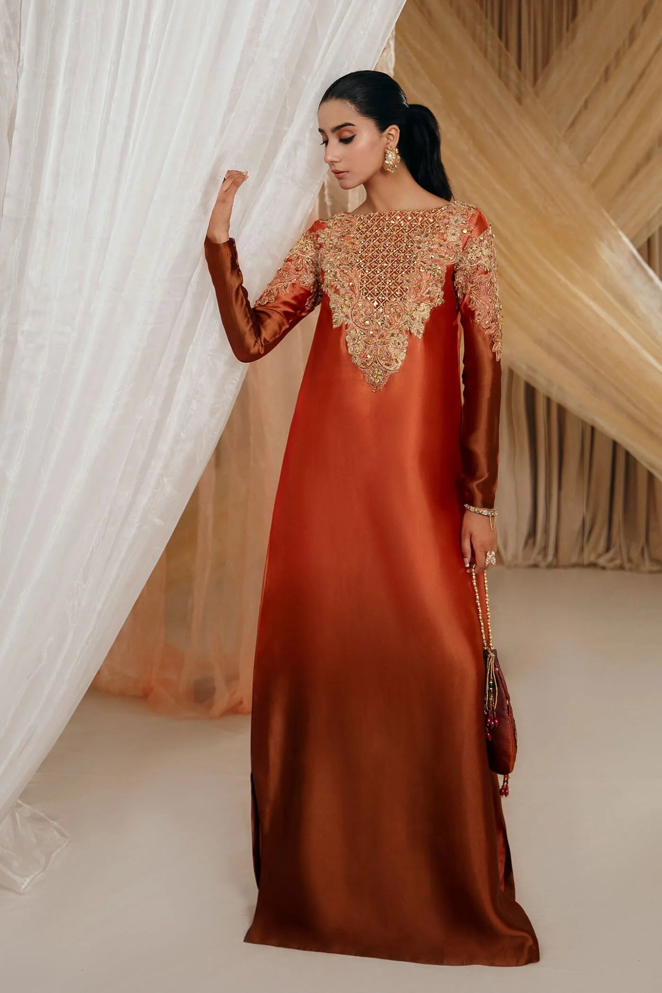 Model wearing Faiza Saqlain's Sunset Glow dress from the Musferah Saad Mystere Eid Collection '24. A stunning Pakistani Eid dress in burnt orange with intricate embroidery, ideal for Pakistani designer clothes lovers in the UK.