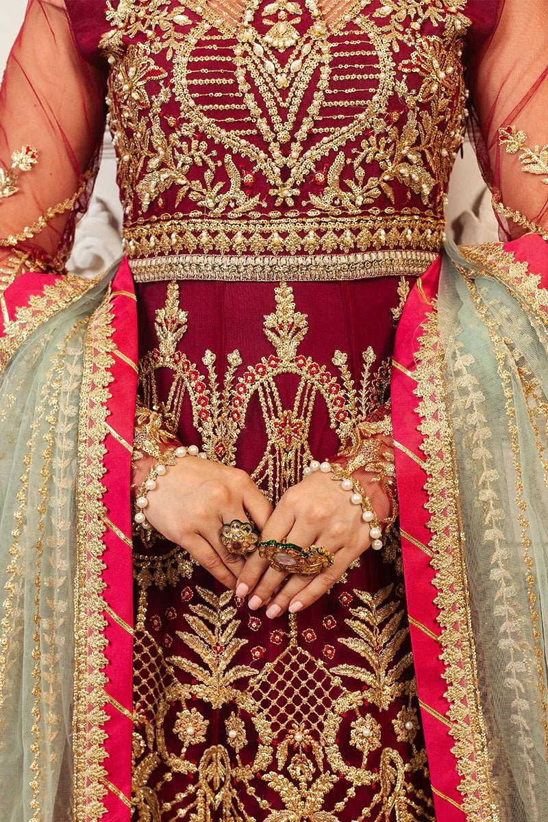 Model wearing a deep red and gold intricately embroidered Asian wedding formal dress, "Scarlet," from Mushq. Pakistani wedding clothes online in the UK.