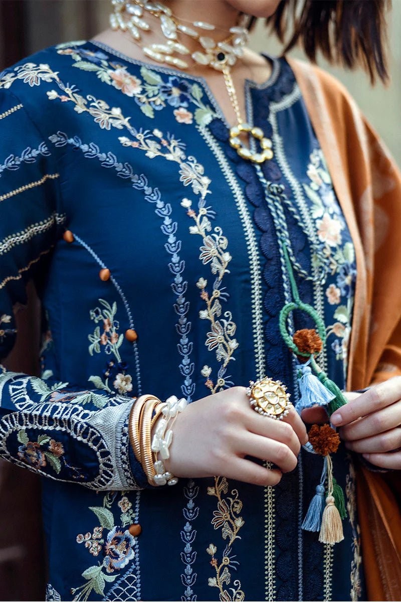 Model wearing Mushq Broadway A Walk to Remember Sweet Surrender, a blue dress with intricate embroidery and an orange shawl, perfect for winter casual wear. Available for Pakistani clothes online in the UK.