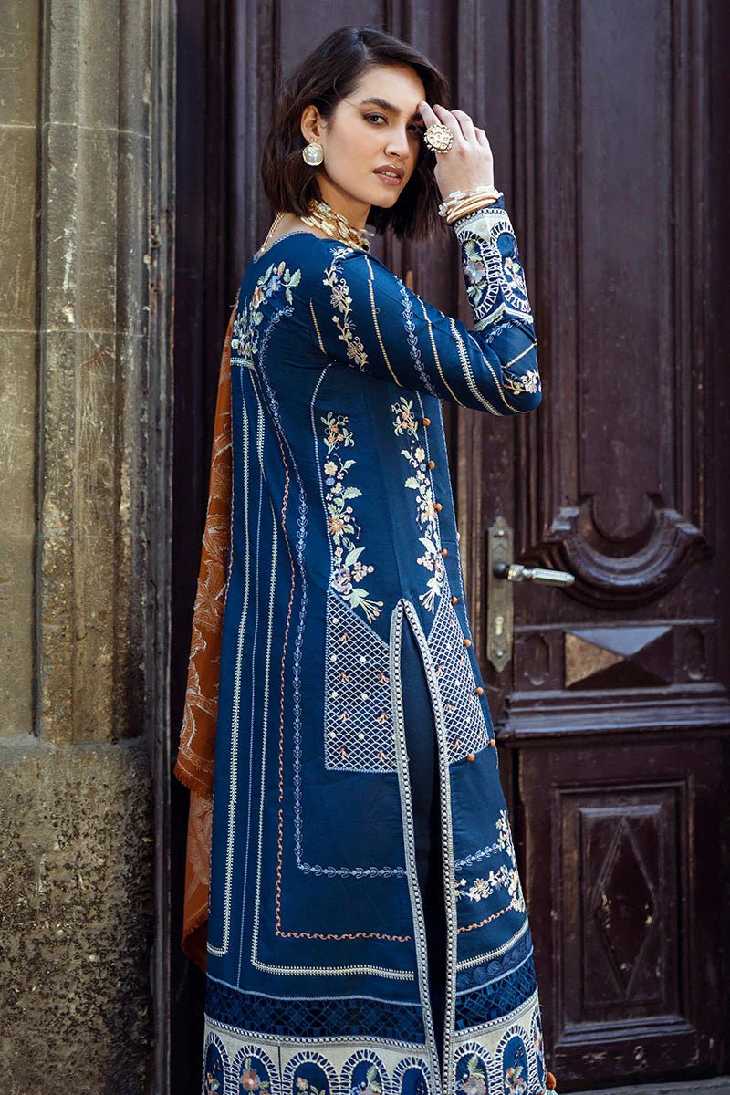 Model wearing Mushq Broadway A Walk to Remember Sweet Surrender, a blue dress with intricate embroidery and an orange shawl, perfect for winter casual wear. Available for Pakistani clothes online in the UK.