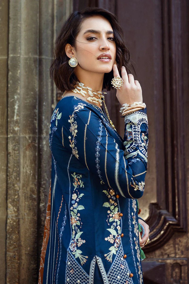 Model wearing Mushq Broadway A Walk to Remember Sweet Surrender, a blue dress with intricate embroidery and an orange shawl, perfect for winter casual wear. Available for Pakistani clothes online in the UK.