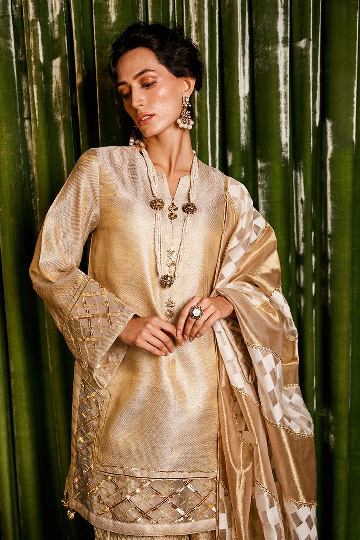 Model wearing a golden Basanti outfit from Mushq with intricate gota detailing, showcasing Pakistani designer clothes online in the UK, perfect for weddings.