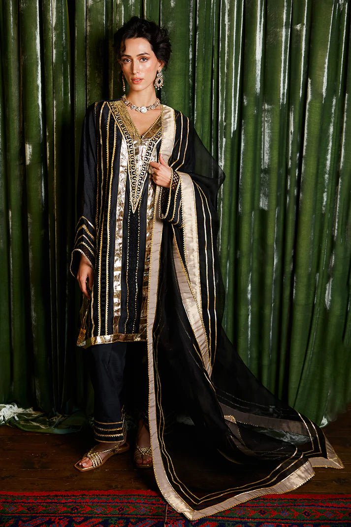 Model wearing a striking black and gold Koyal dress from Mushq with intricate gota detailing, ideal for Pakistani weddings, available online in the UK.