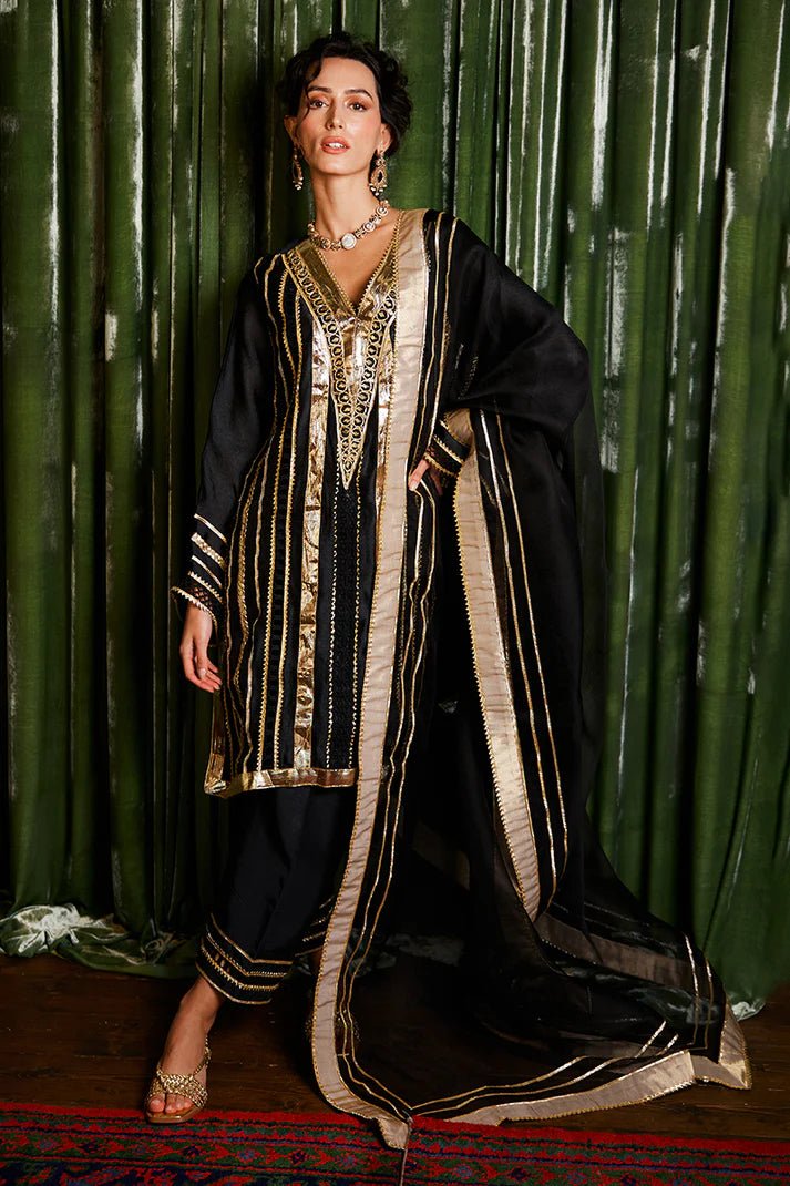 Model wearing a striking black and gold Koyal dress from Mushq with intricate gota detailing, ideal for Pakistani weddings, available online in the UK.