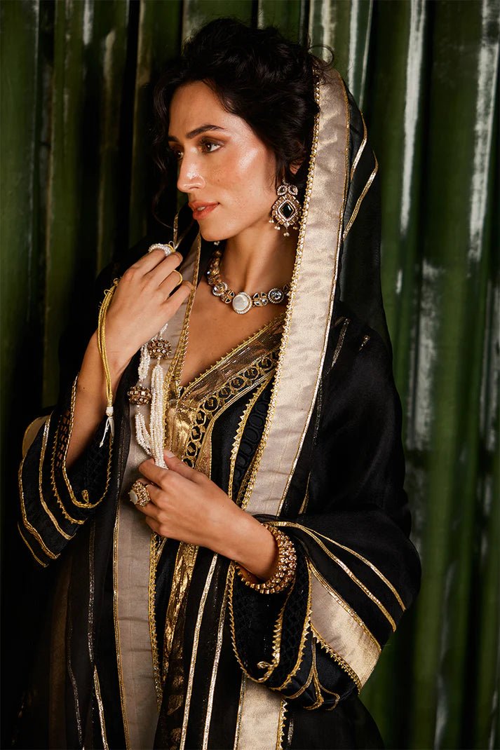 Model wearing a striking black and gold Koyal dress from Mushq with intricate gota detailing, ideal for Pakistani weddings, available online in the UK.