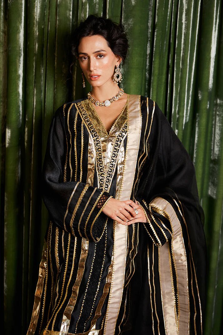 Model wearing a striking black and gold Koyal dress from Mushq with intricate gota detailing, ideal for Pakistani weddings, available online in the UK.