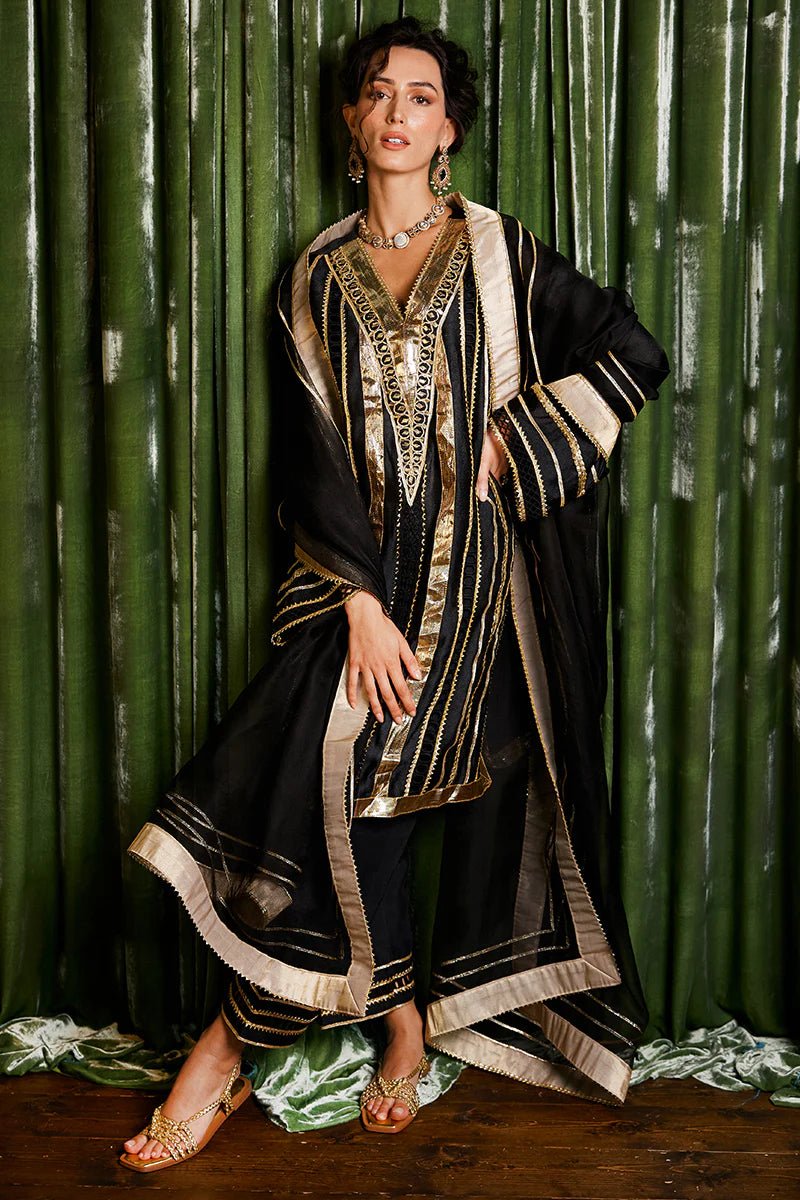 Model wearing a striking black and gold Koyal dress from Mushq with intricate gota detailing, ideal for Pakistani weddings, available online in the UK.