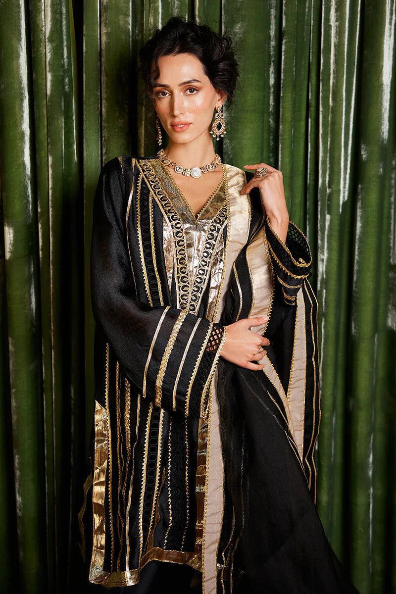 Model wearing a striking black and gold Koyal dress from Mushq with intricate gota detailing, ideal for Pakistani weddings, available online in the UK.