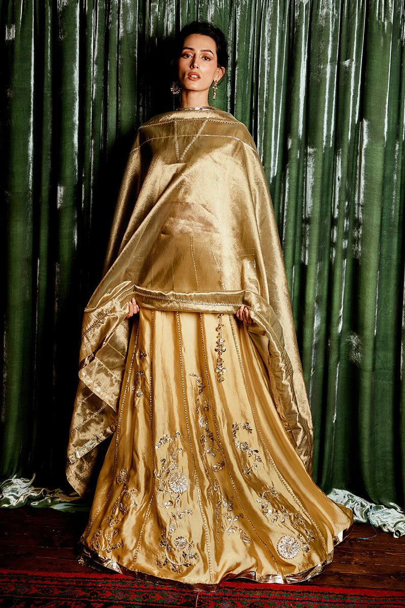 Model wearing a golden Suraj Mukhi lehenga from Mushq, adorned with intricate gota work, perfect for weddings, showcasing Pakistani designer clothes online in the UK.