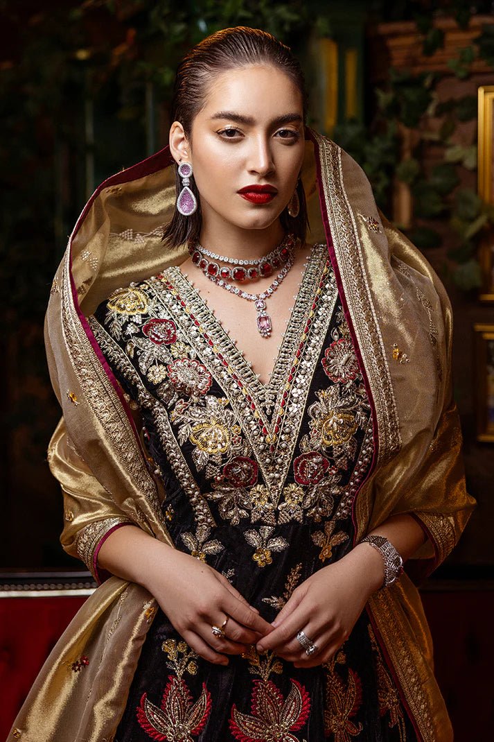 Model wearing Mushq DEJA VU - VELVET '24 Whispers of Yesterday, a black velvet gown with intricate gold and red floral embroidery, styled with a luxurious golden shawl. Ideal for winter weddings, available for Pakistani clothes online in the UK.