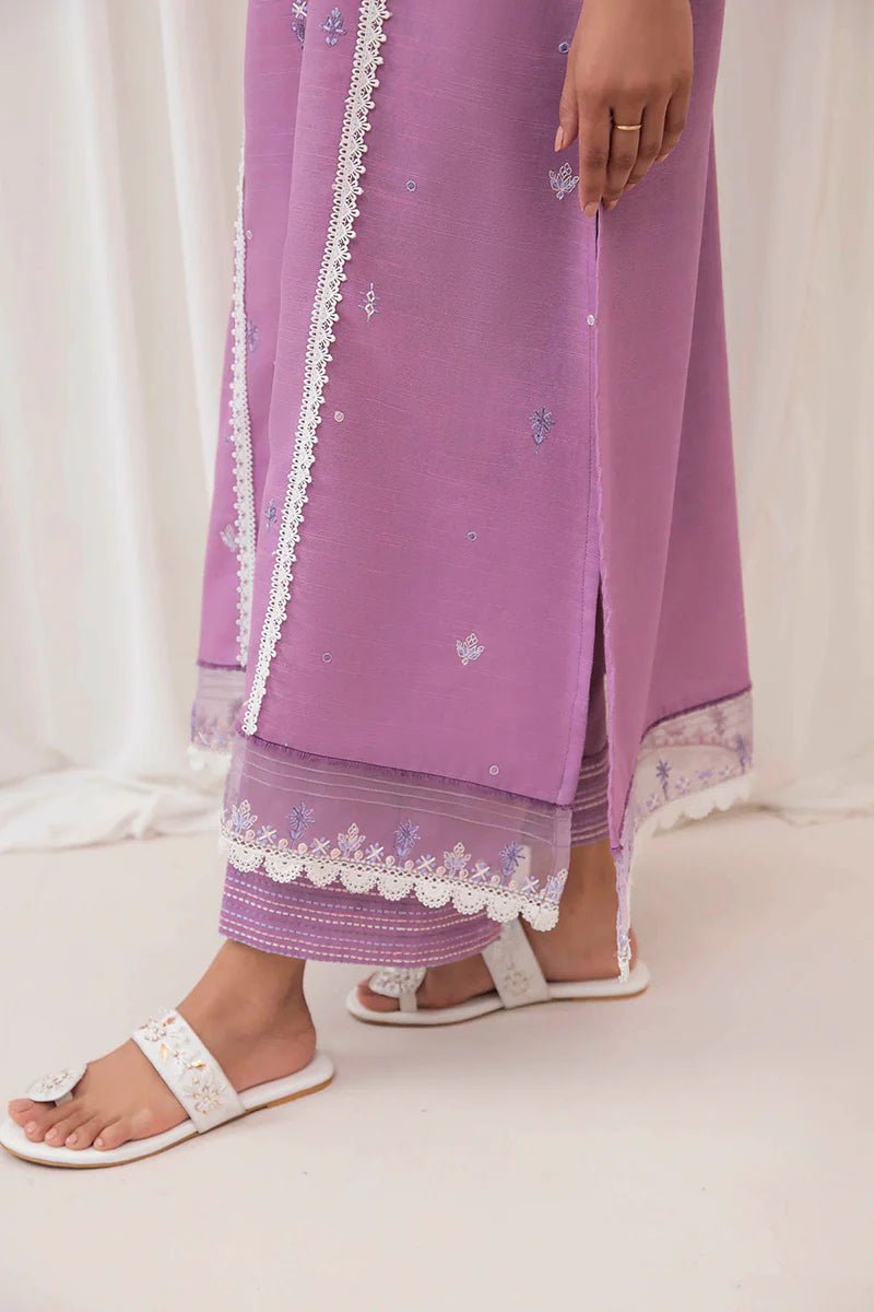 Model wearing Mushq Wisteria Winter Basic Pret '24 Frost Flair, a lavender dress adorned with white lace details, perfect for winter casual wear. Available for Pakistani clothes online in the UK.